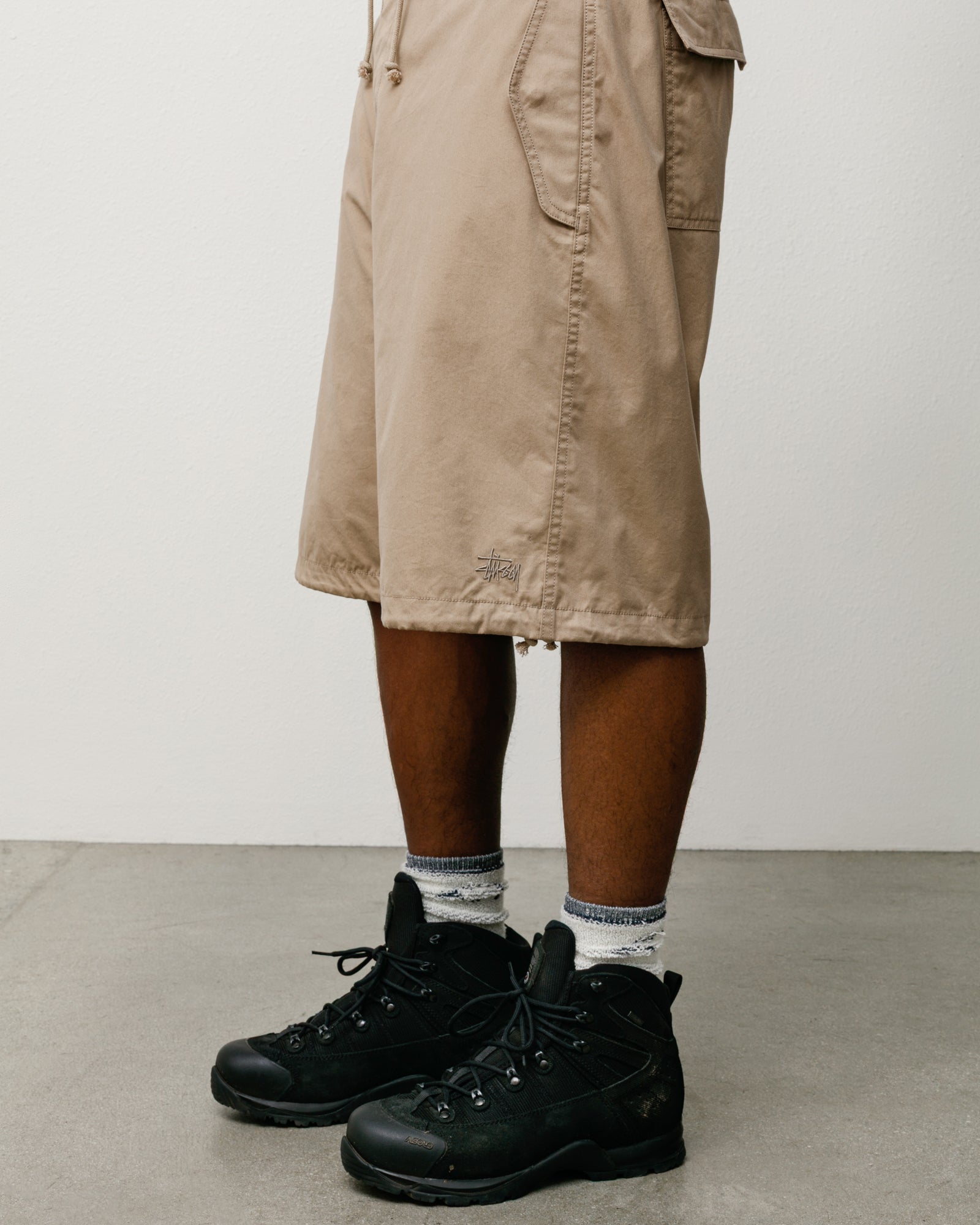 Khaki baggy cotton-nylon Surplus Short with drawcord hem and Stüssy logo, modelled with boots