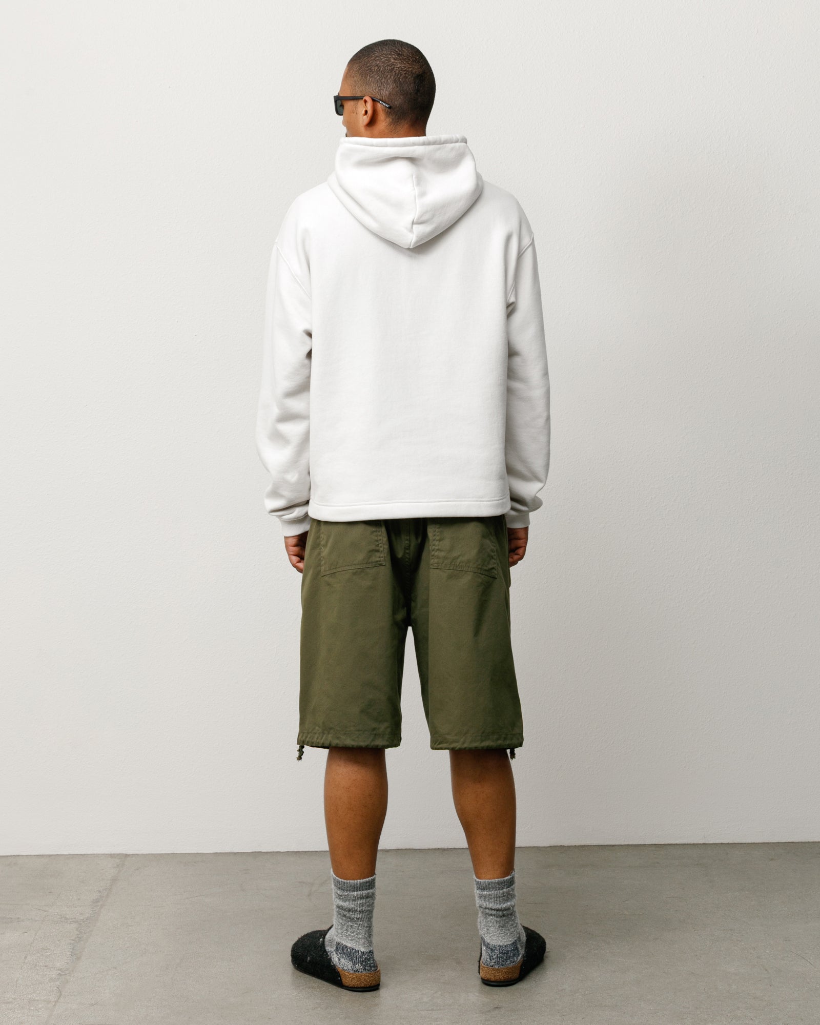 Olive surplus shorts with rear patch pockets and drawcord hems, shown on model from the back.