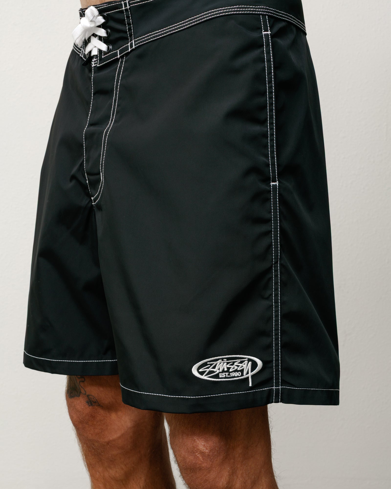 Black board shorts with white contrast stitching, lace-up waist and Stüssy logo