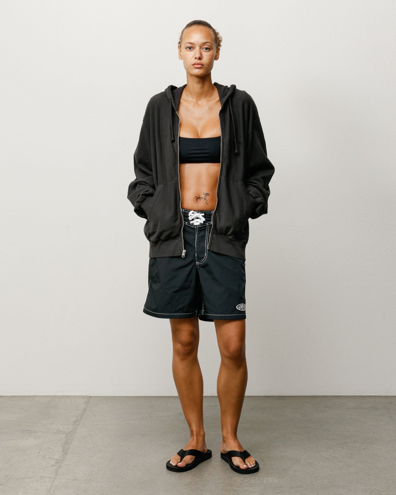 Black unisex board short with laced drawcord and contrast stitching, worn by model.
