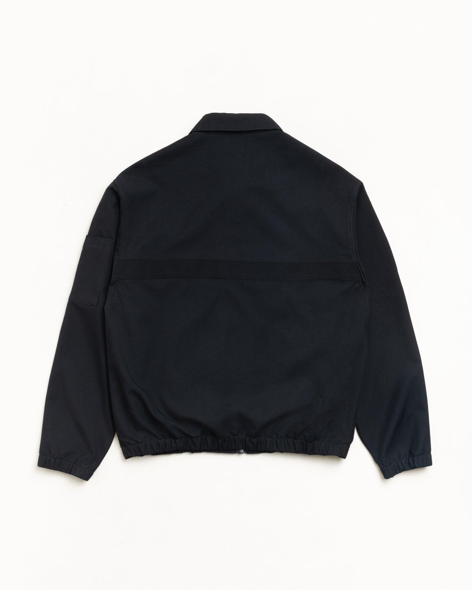 Back view of black unisex mechanic jacket with long sleeves, elastic hem and sleeve pocket