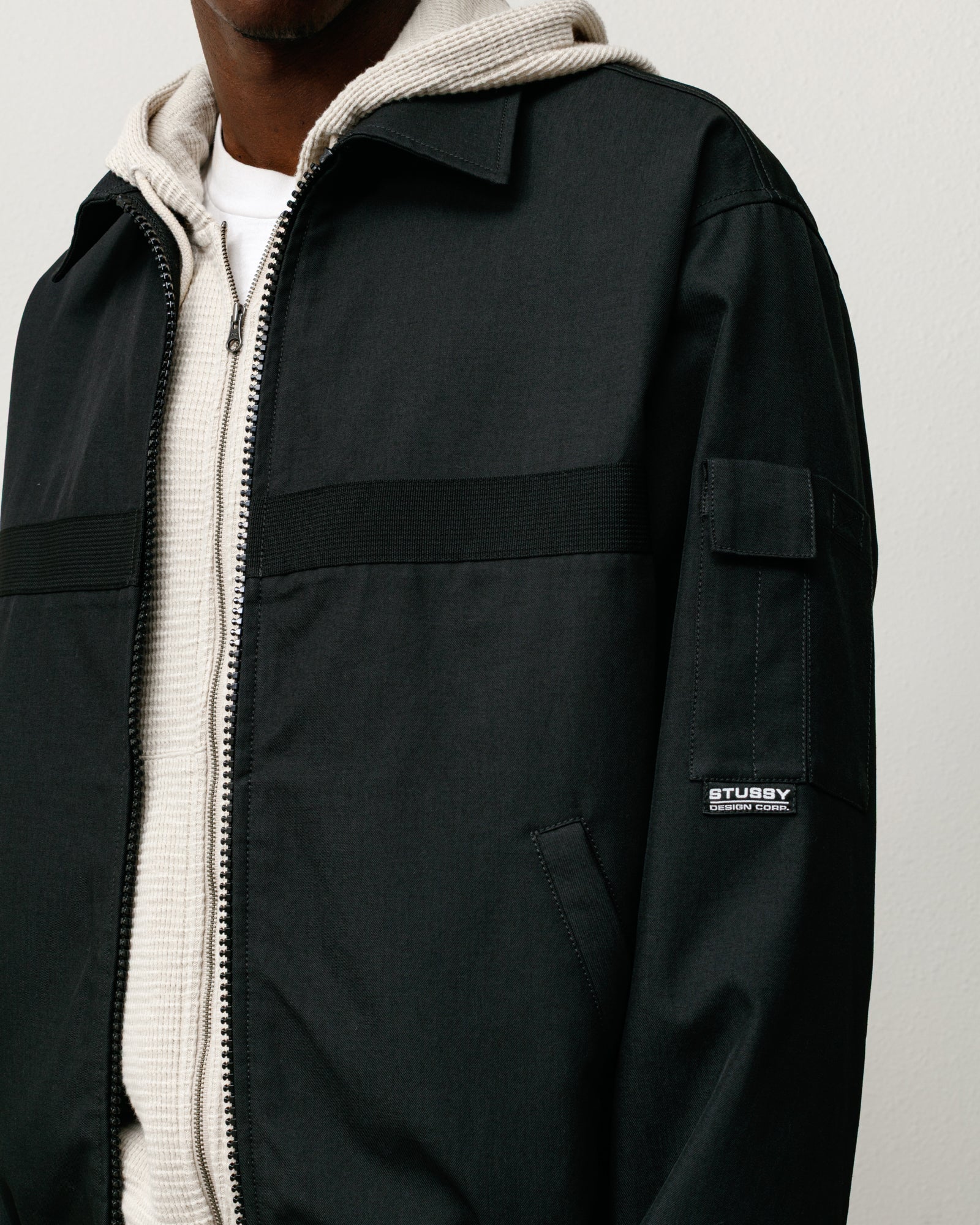 Black mechanic jacket with zip front, angled welt pockets, webbing band and sleeve patch label