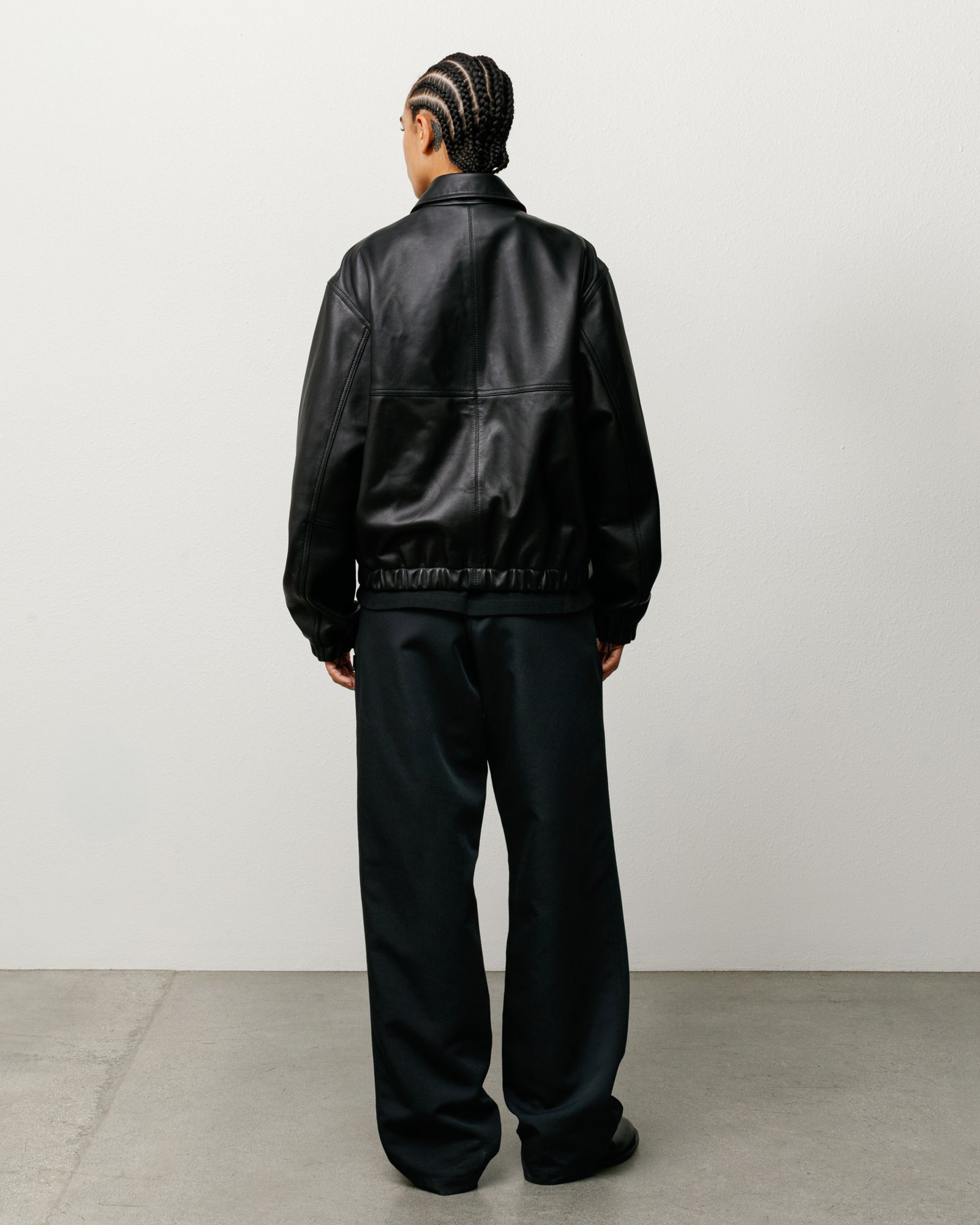 Black leather work jacket, back view on model, relaxed fit with elastic hem and long sleeves