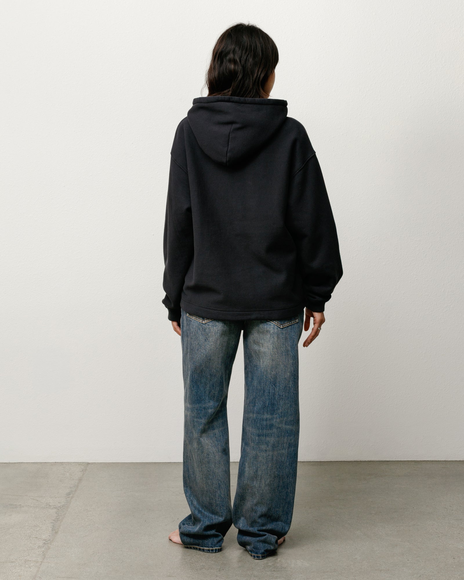 Black unisex pullover hoodie, back view on model with relaxed fit and roomy hood.