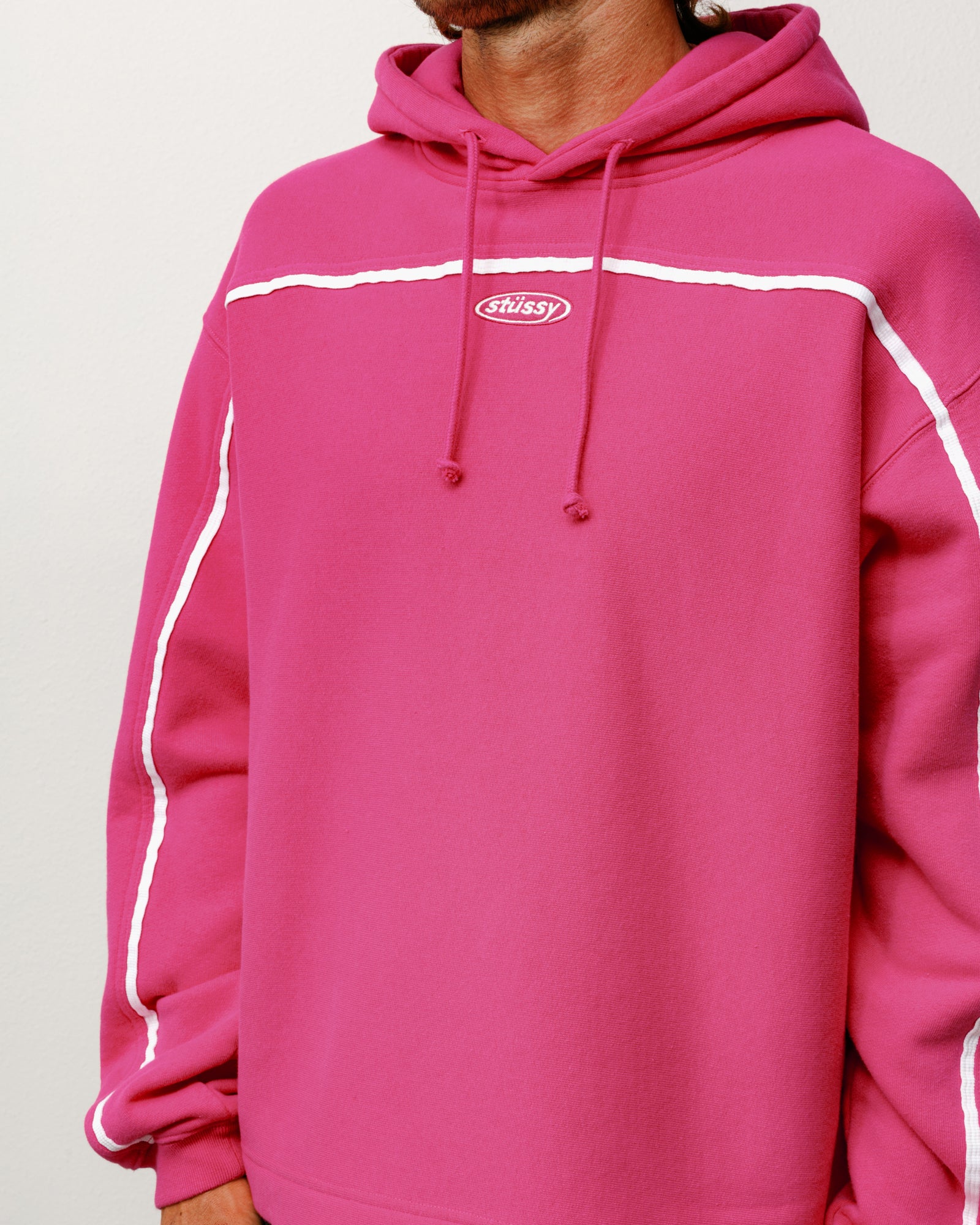 Pink pullover hoodie with white contrast piping, long sleeves and oval chest logo embroidery
