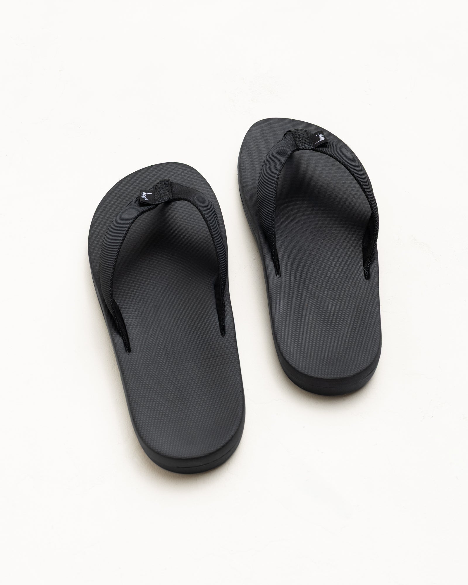 Black rubber flip-flops with wide nylon webbing straps, unisex, top view on white background